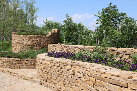 Aménagement paysager extérieur avec murets en pierre naturelle calcaire beige, construction de terrasses étagées et jardinières intégrées