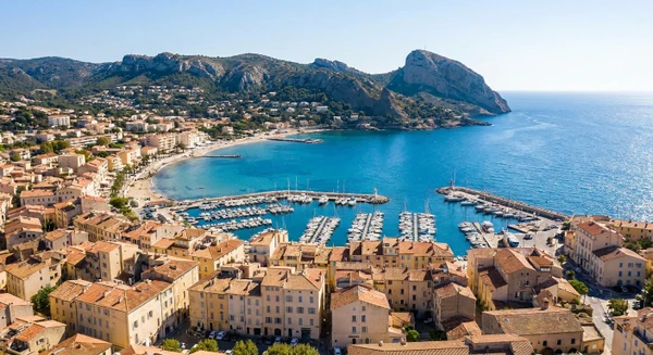 Vue aérienne ou panoramique de La Ciotat montrant la commune depuis une perspective élevée avec ses caractéristiques côtières provençales : le littoral méditerranéen, le port ou les plages, les bâtiments et quartiers résidentiels, les collines ou massifs rocheux en arrière-plan. Image claire, professionnelle et réaliste représentant le cadre géographique de cette commune des Bouches-du-Rhône. Sans texte, logo ou filigrane visible.